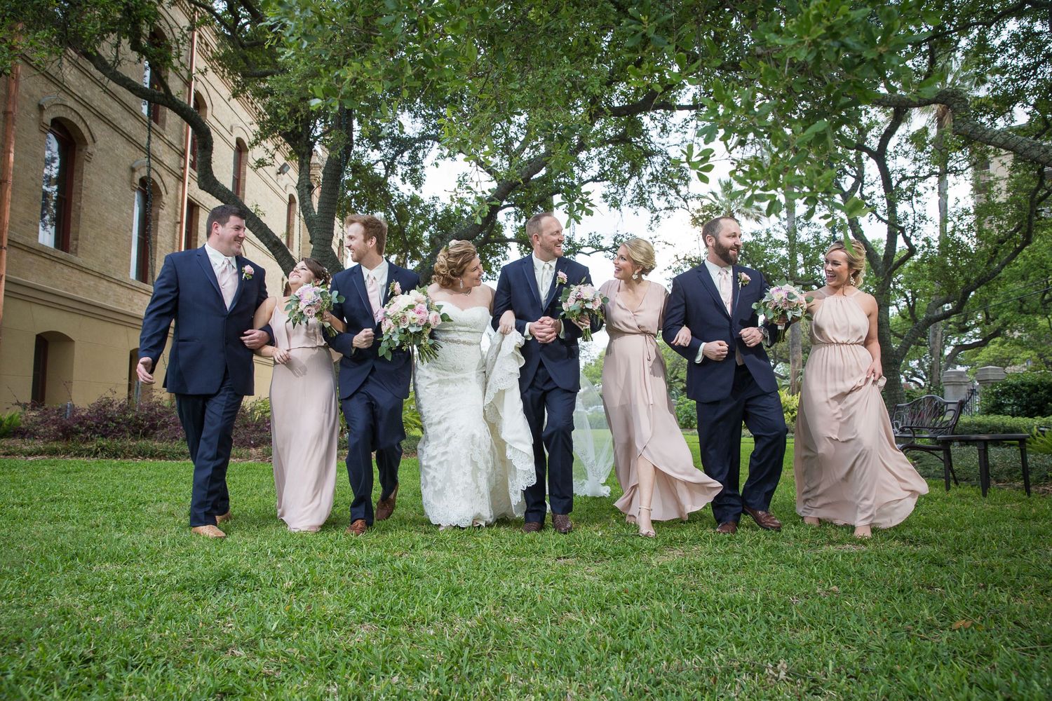 Wedding party walking together on green lawn outside historic building.