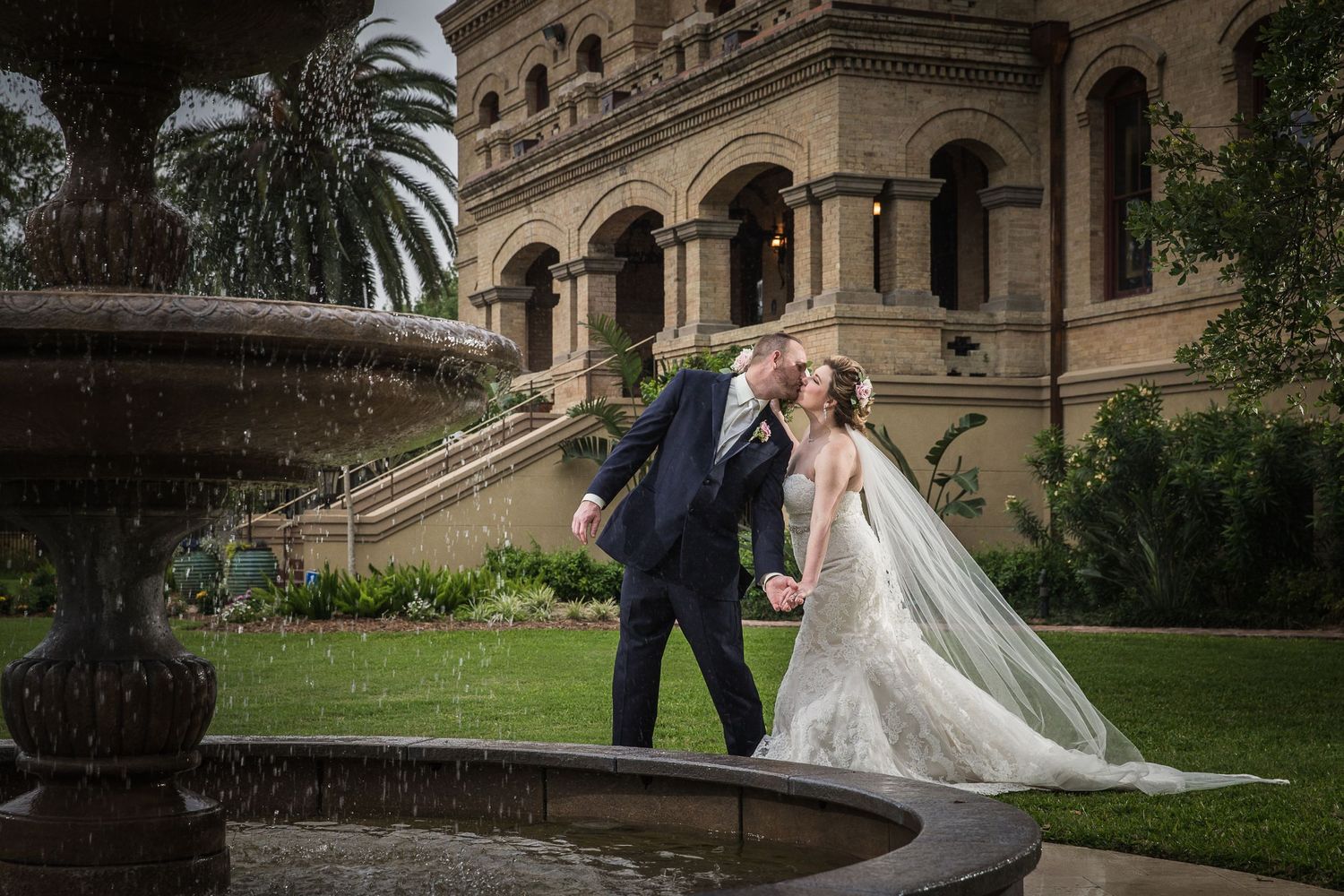 Romantic moment by fountain outside historic stone building.