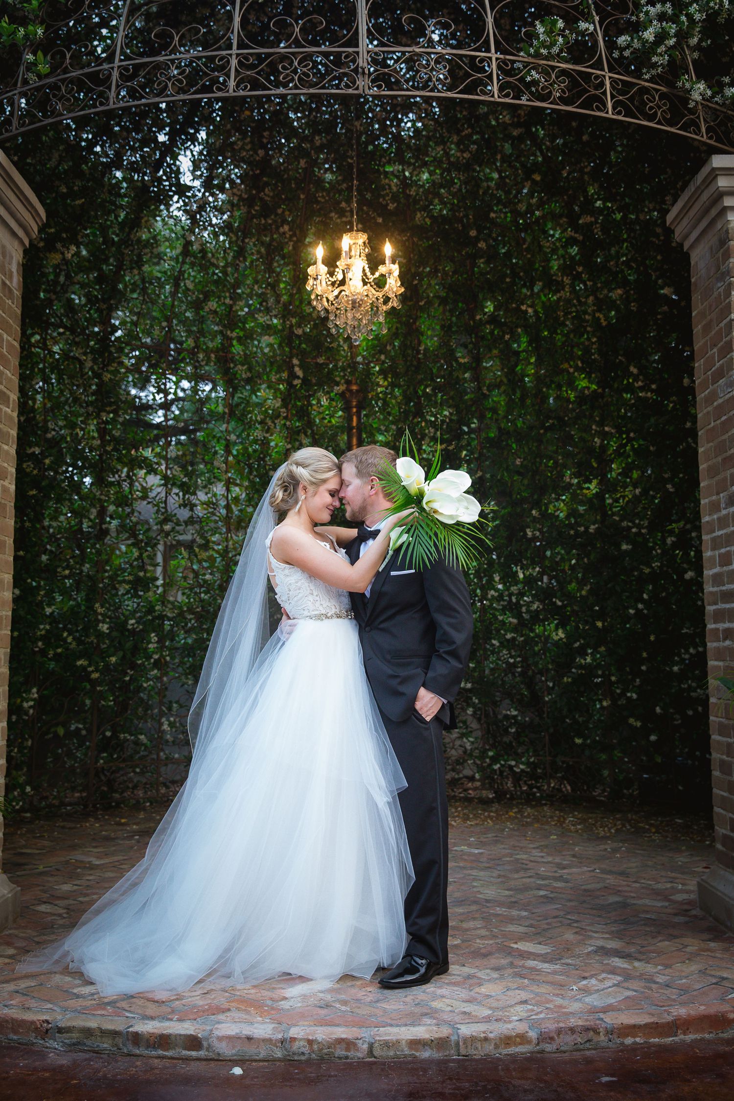 Couple sharing romantic kisses under an elegant garden archway with twinkling lights.