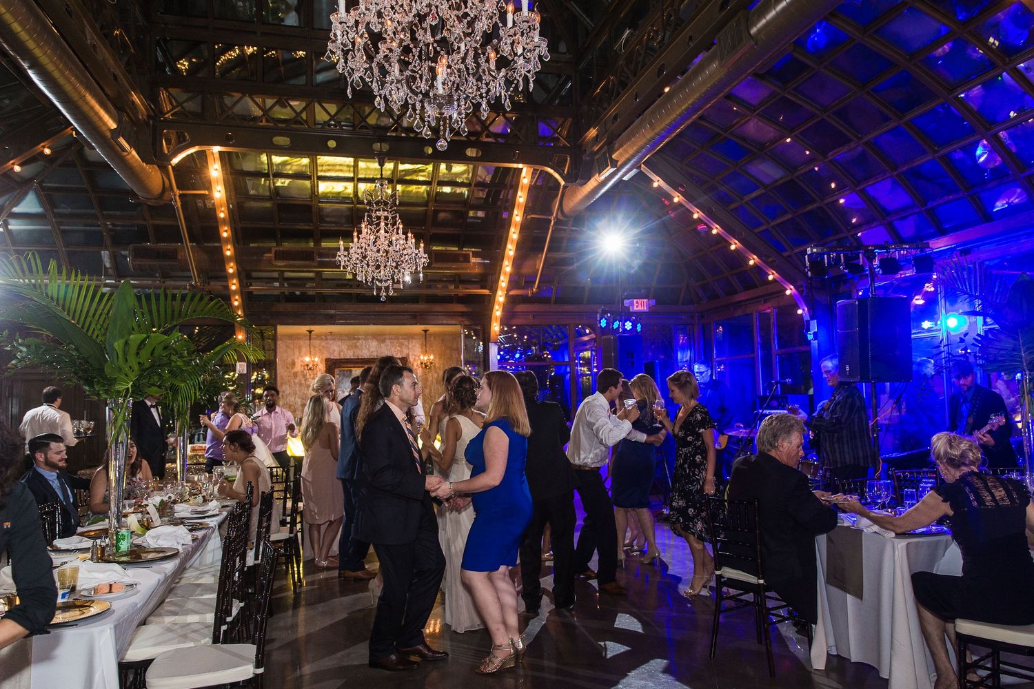 Wedding reception venue illuminated with dramatic blue lighting and crystal chandeliers.