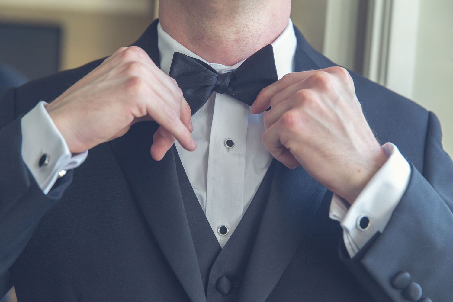 Groom adjusting his bowtie in preparation for the wedding ceremony.