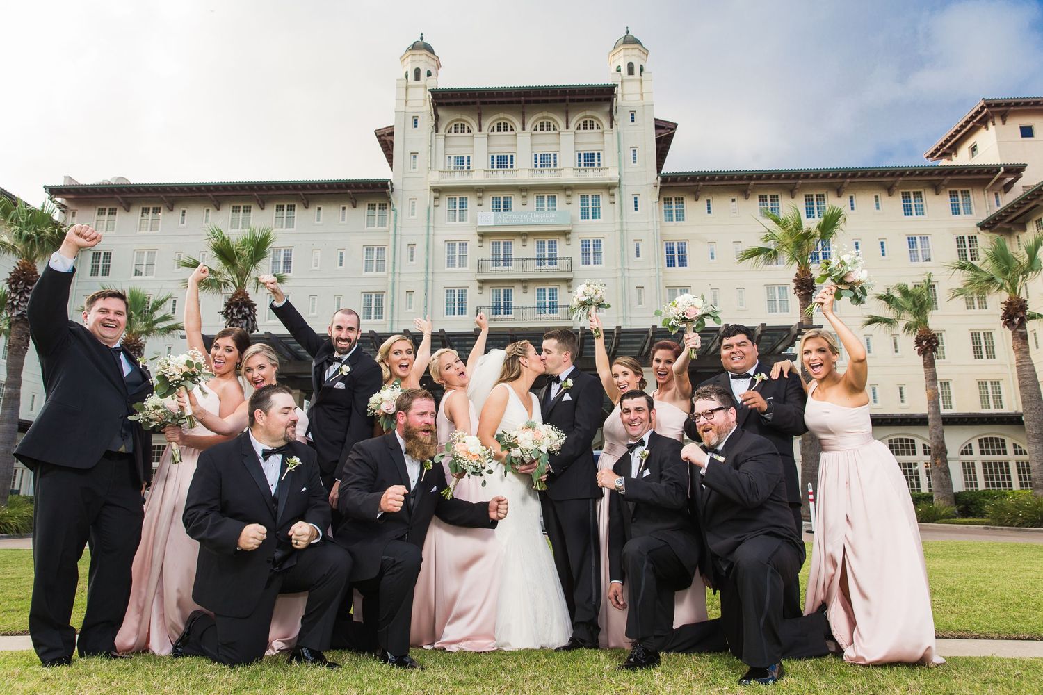 Wedding party in formal attire posing outside a grand hotel building.