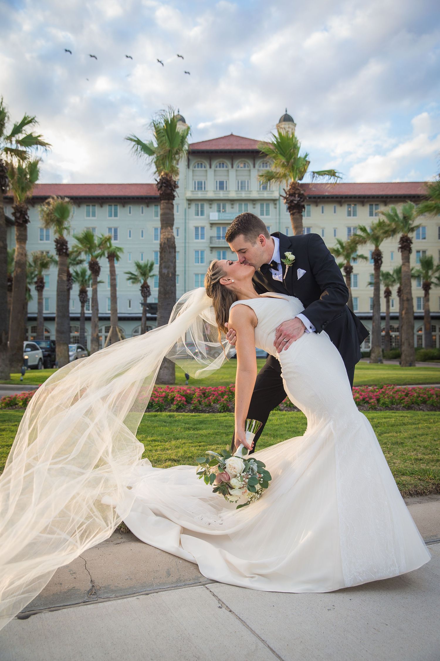 Romantic wedding portraits with flowing veil against coastal hotel backdrop.