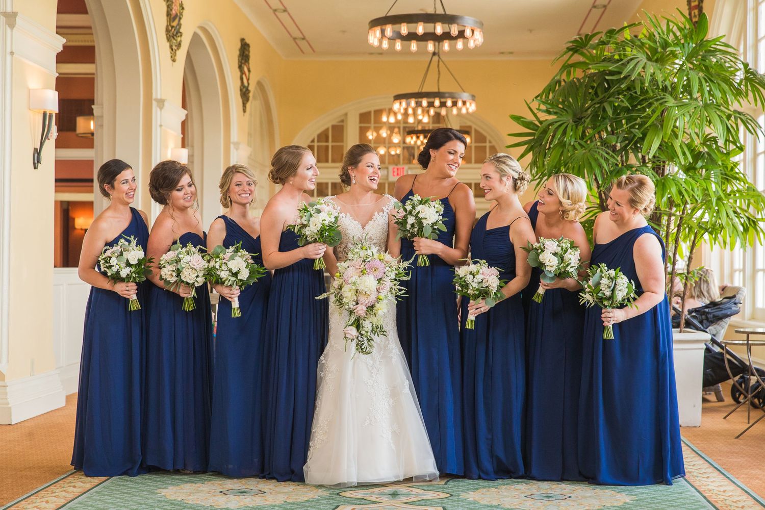 Wedding party in navy blue dresses and suits lined up for formal photos in an elegant venue.