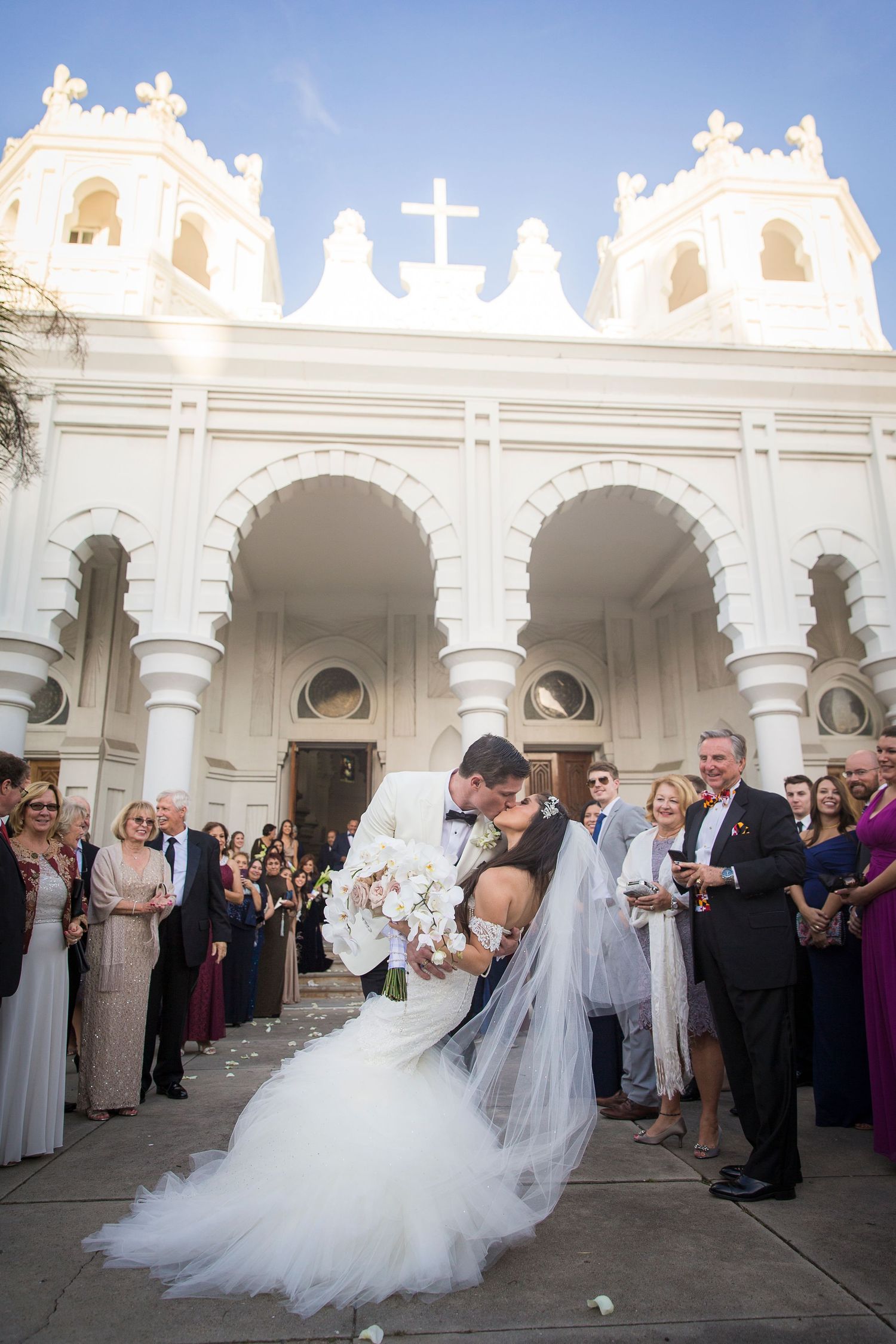 Bride and groom dancing surrounded by guests at white Spanish colonial style venue.