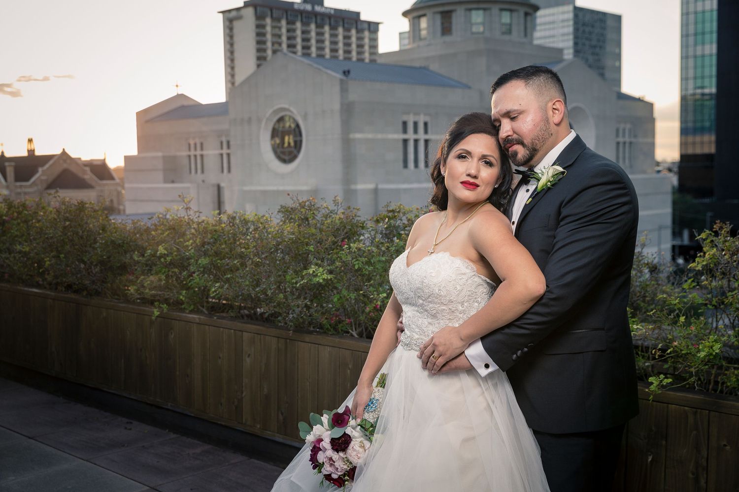Wedding couple poses against urban cityscape backdrop during golden hour.