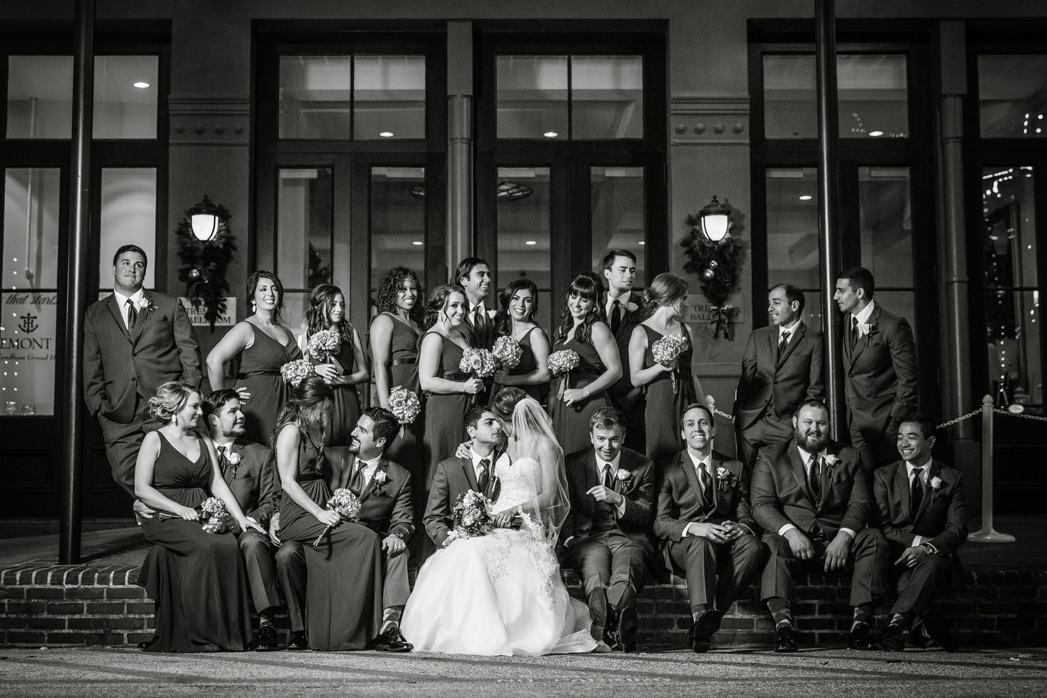 Black and white photo of wedding party lined up along historic storefront buildings.