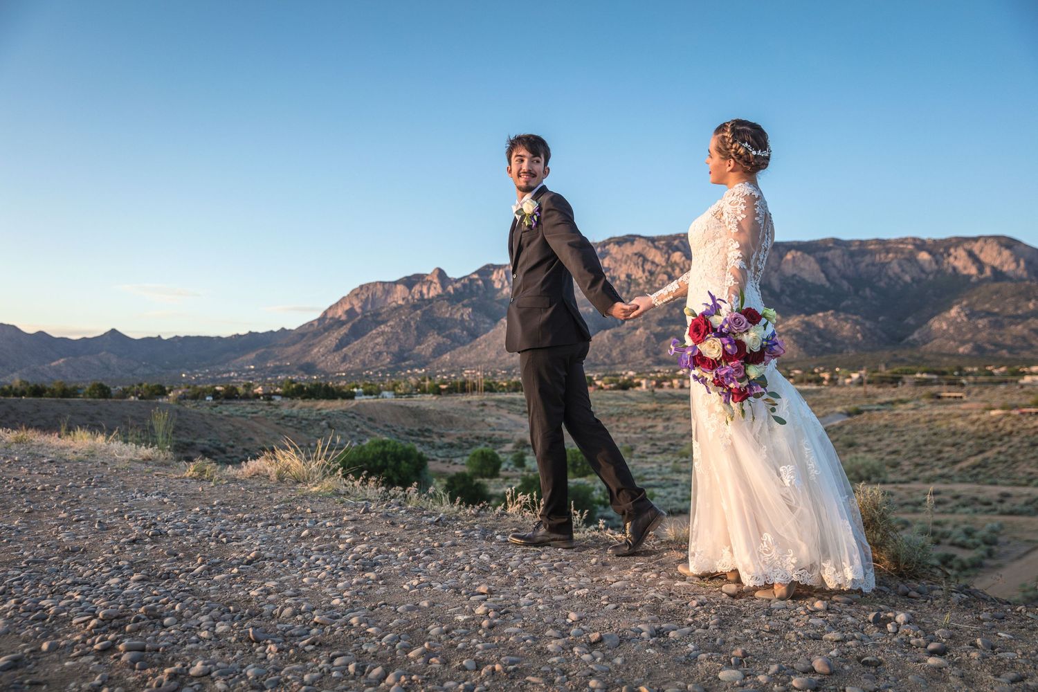 Couple poses on rocky terrain with dramatic mountain landscape behind them.