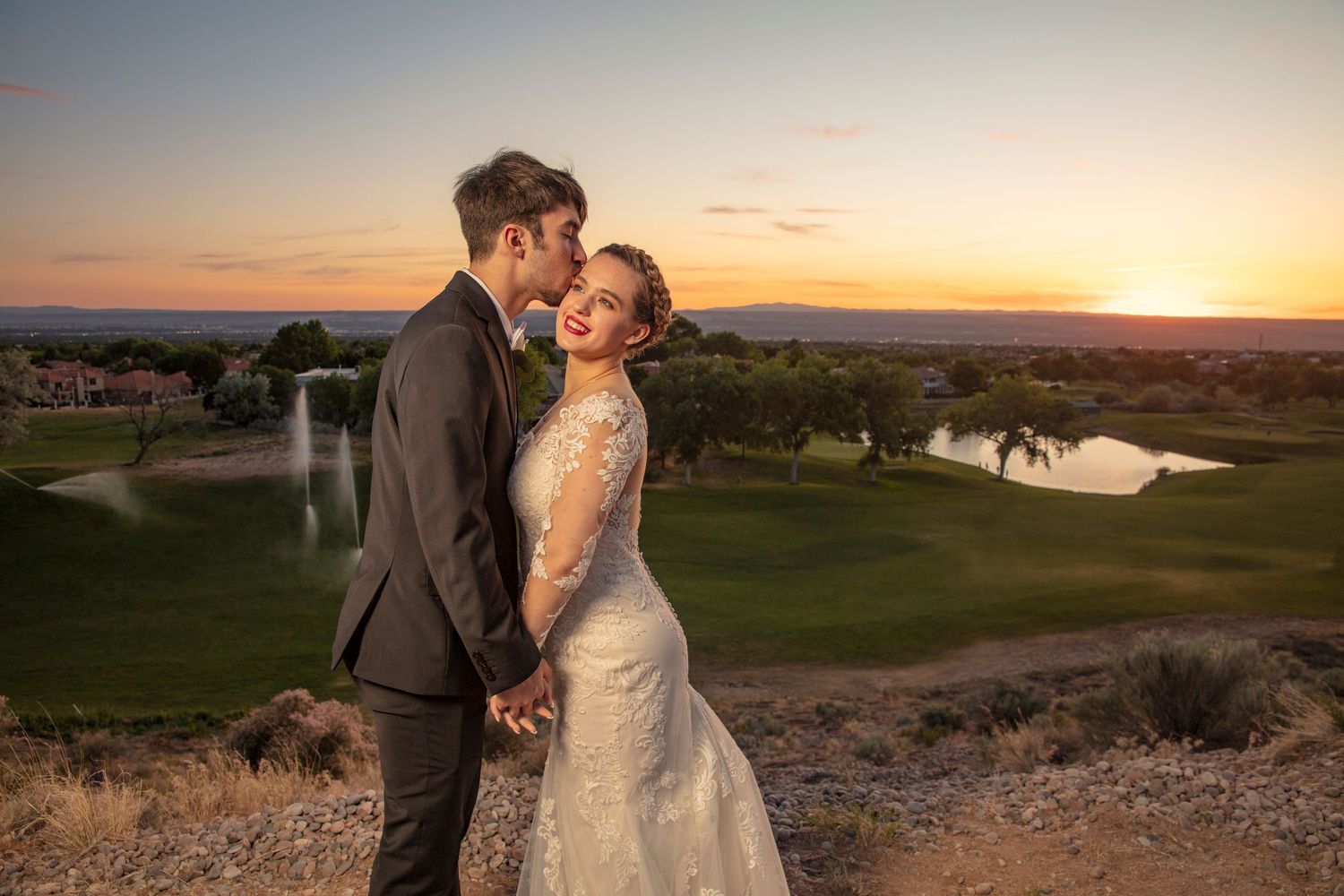 Wedding couple shares intimate moment against stunning desert sunset landscape.