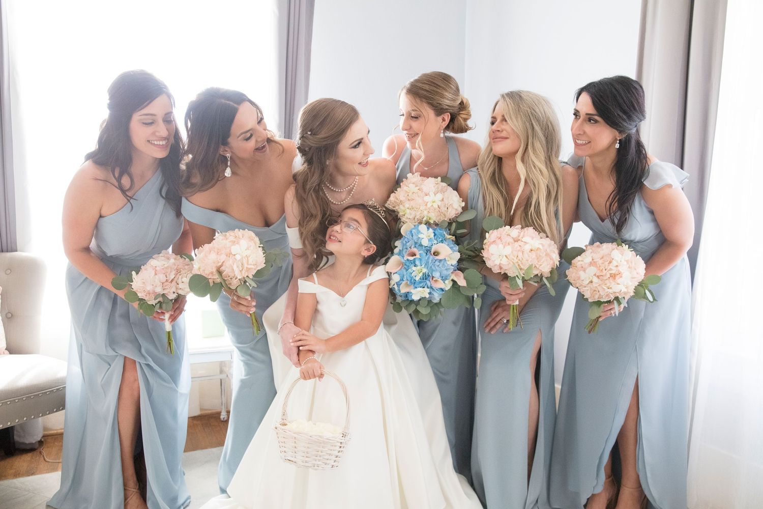 Wedding party in light blue bridesmaid dresses posing together with bouquets.