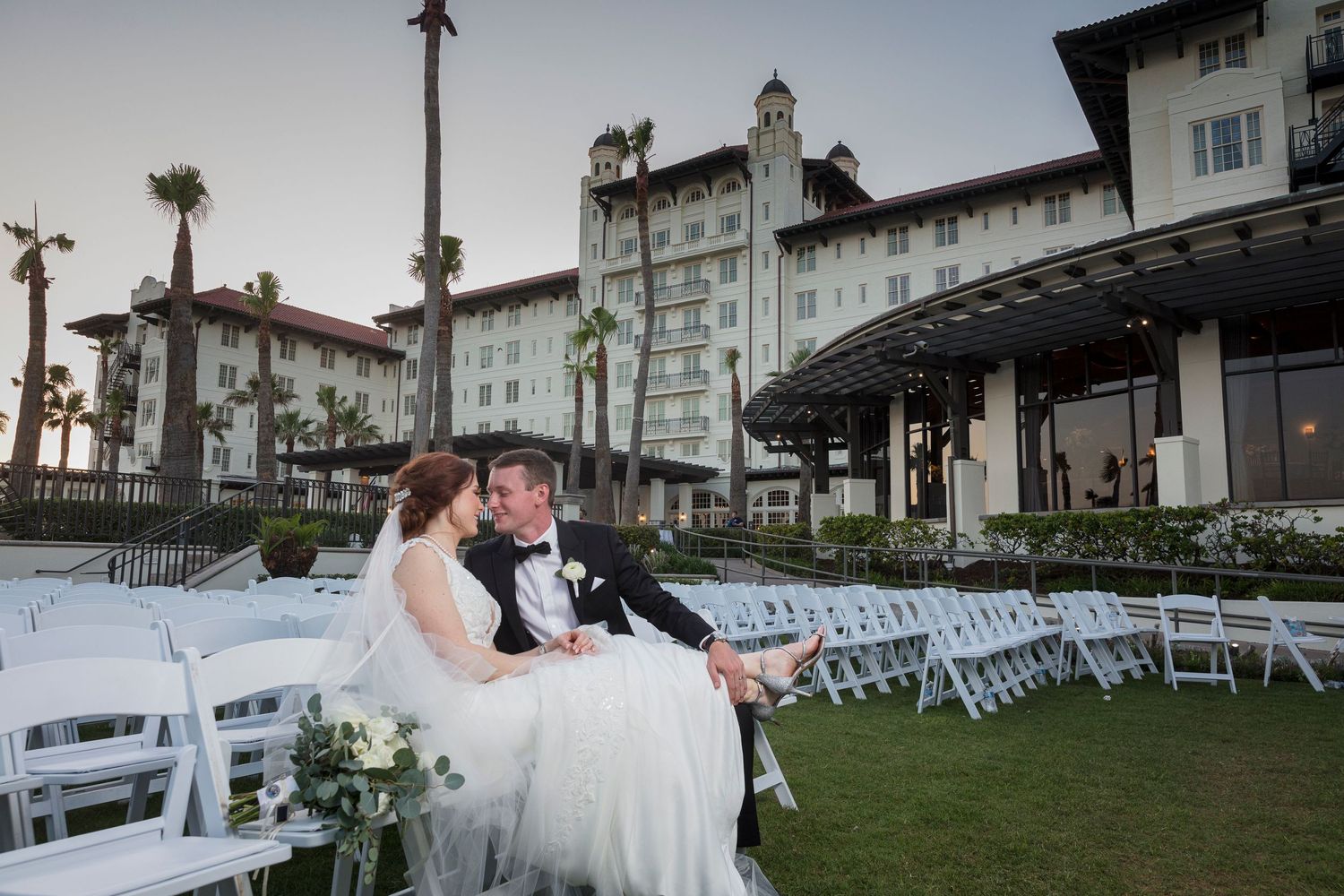 Outdoor wedding ceremony setup with white chairs and ocean view at sunset.