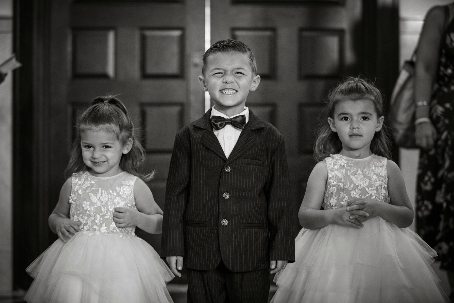 Young attendants in formal wear pose in a classic black and white wedding portrait.