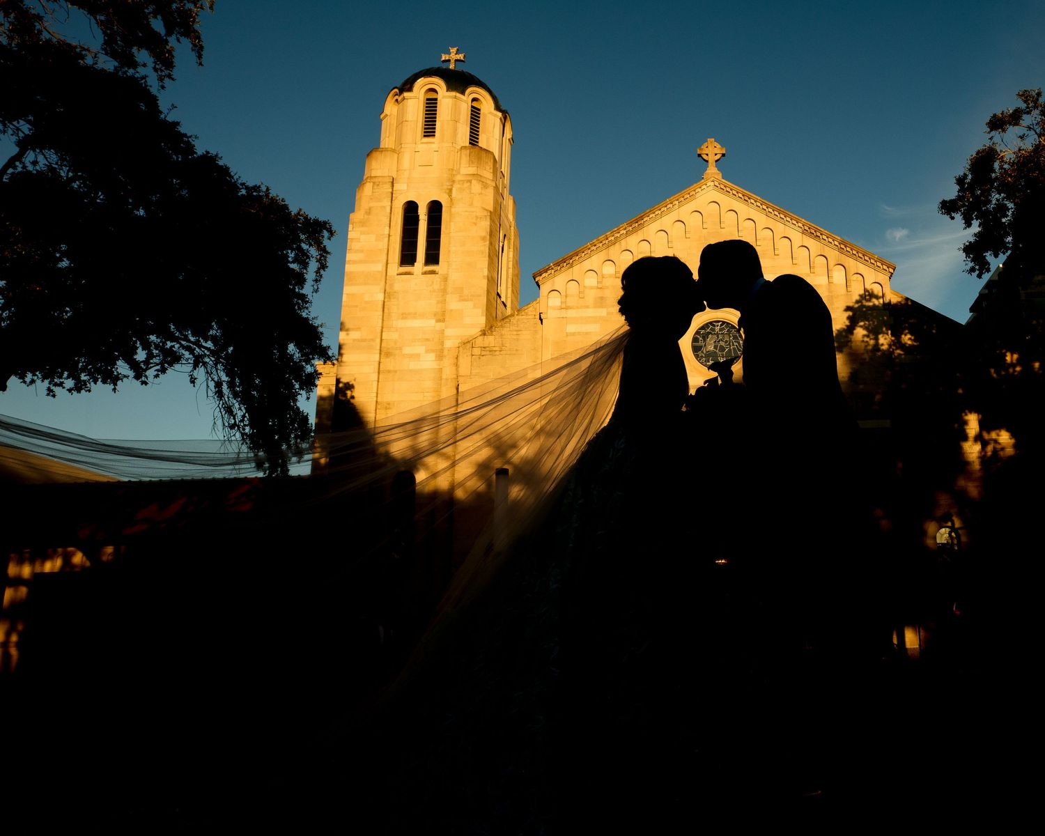 Church steeple silhouetted against a deep blue dusk sky with golden sunlight.