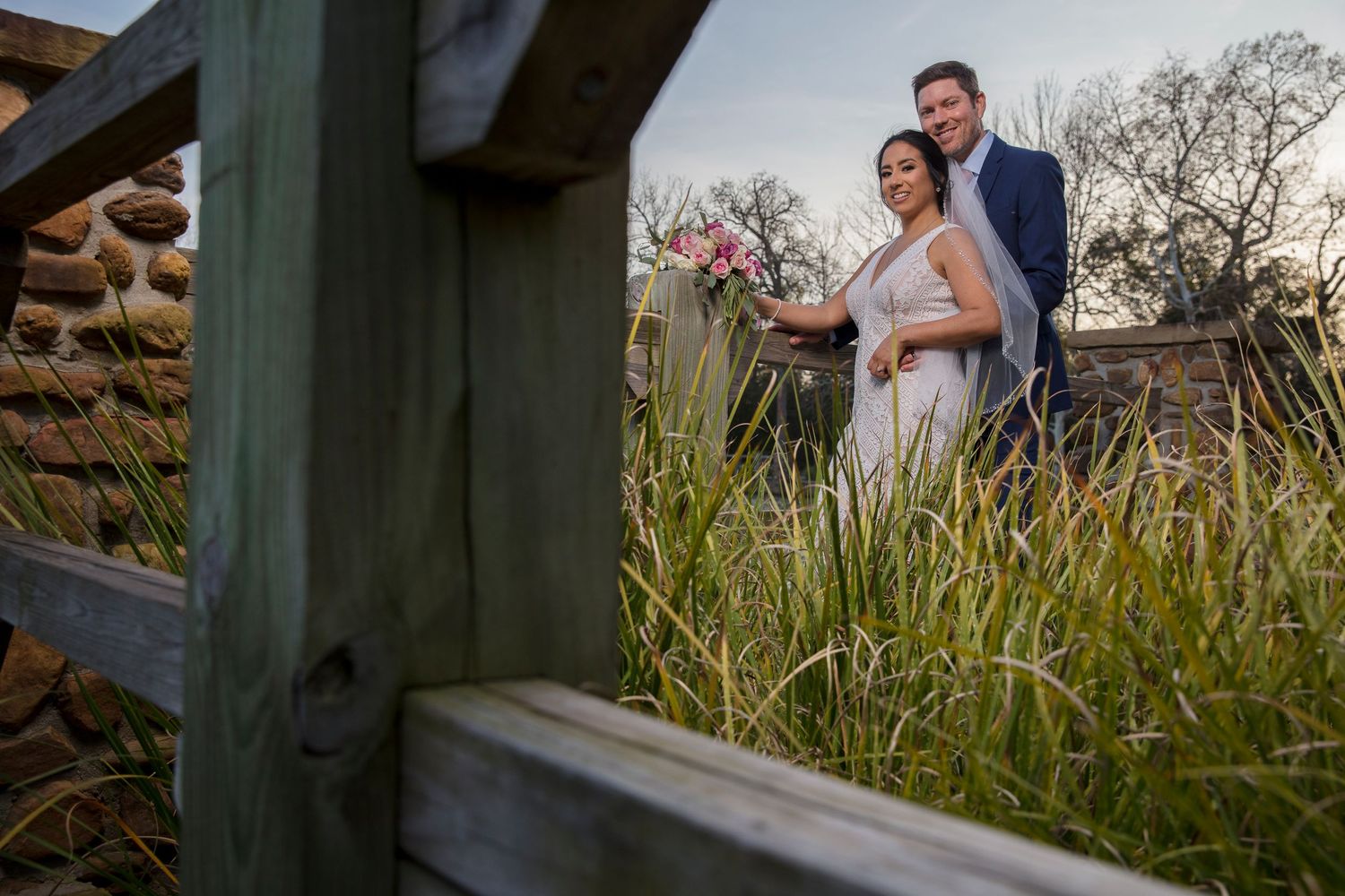 Newlyweds pose together against rustic wooden backdrop in outdoor setting.