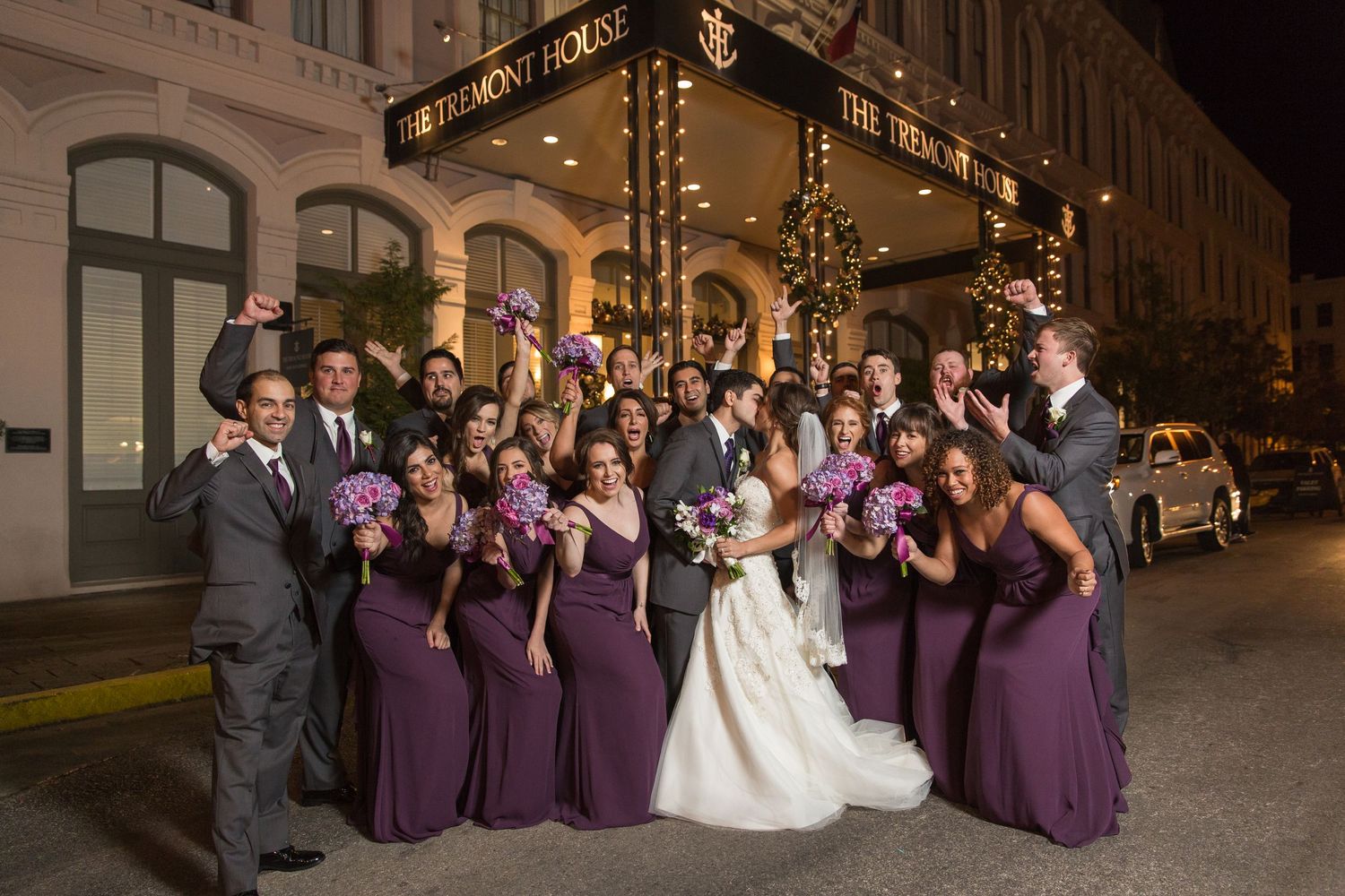 Wedding party in purple dresses posing outside historic architecture at night.