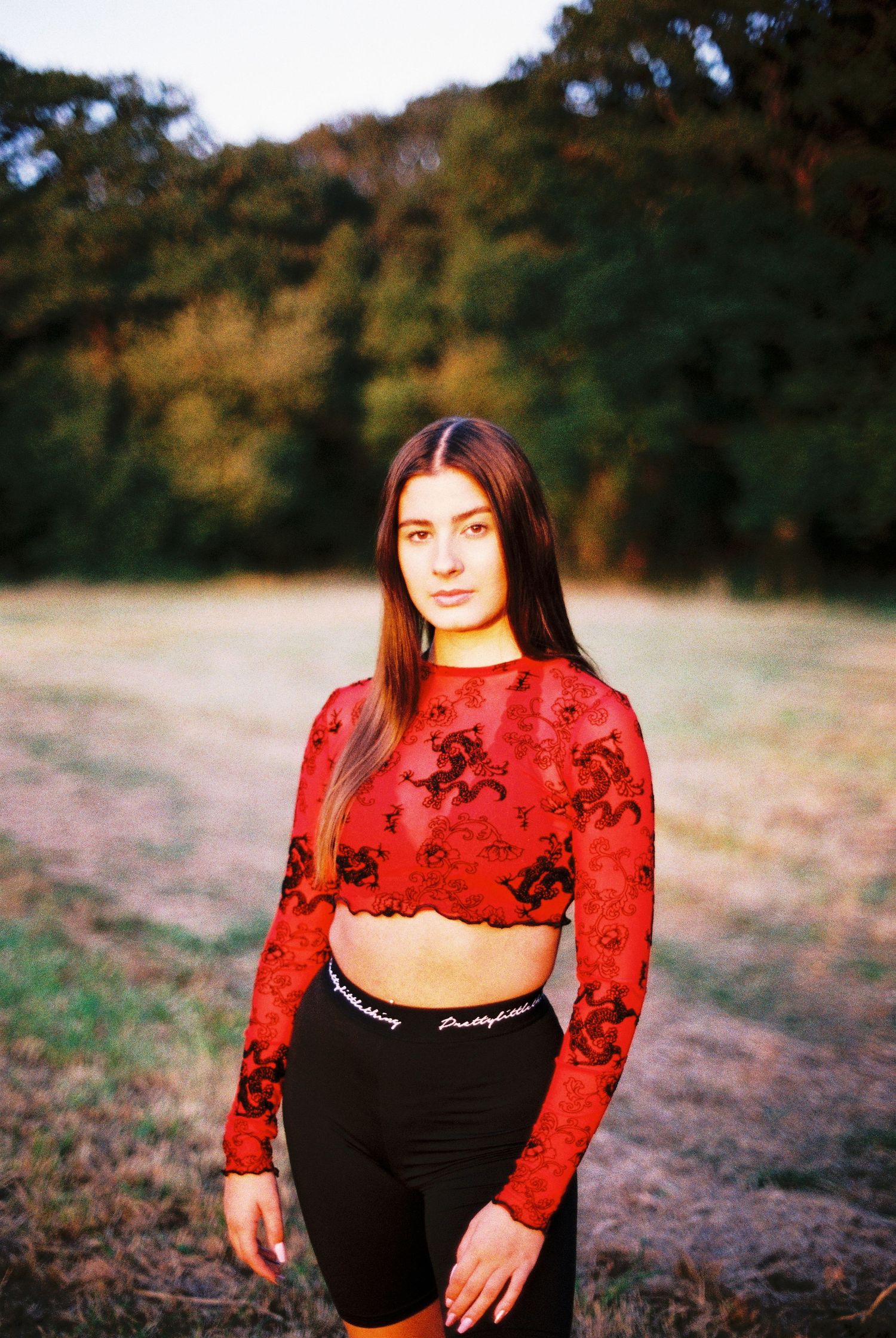 Athletic figure in red floral crop top and black leggings posing outdoors.