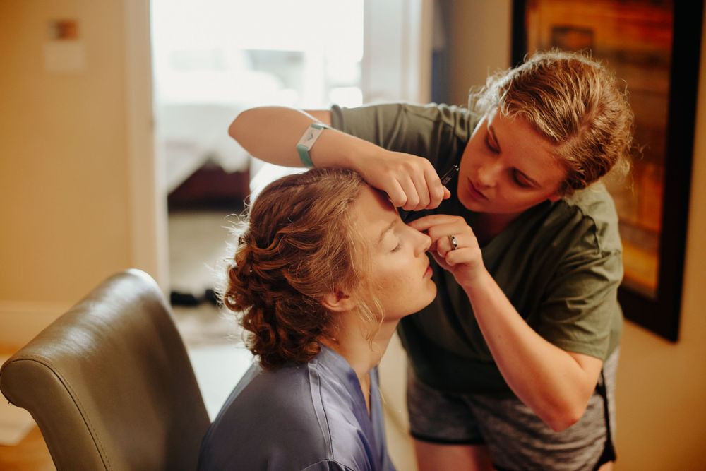 Makeup artist applying finishing touches to bride before wedding ceremony.