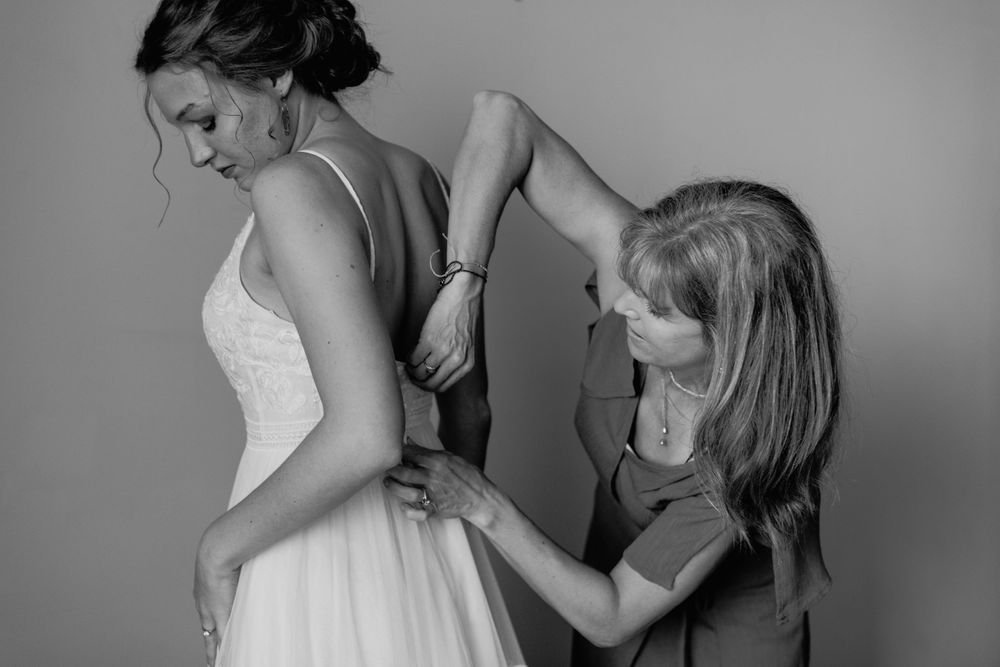 Black and white photo of bridesmaid buttoning bride's wedding dress.