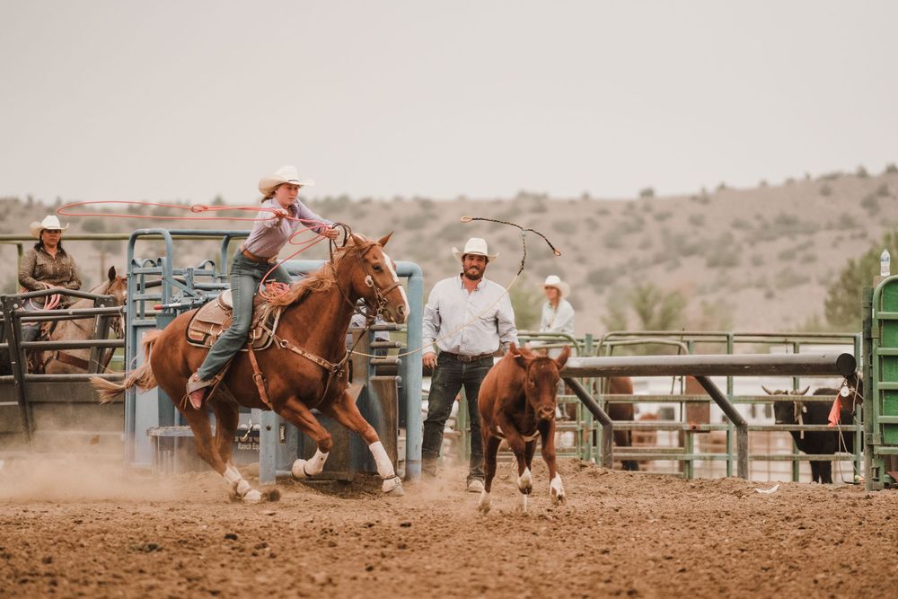 Wide panoramic view of a desert rodeo arena with riders competing.
