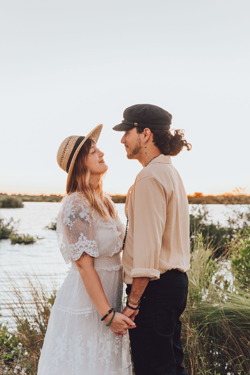 Romantic couple in vintage attire pose by lake during sunset.