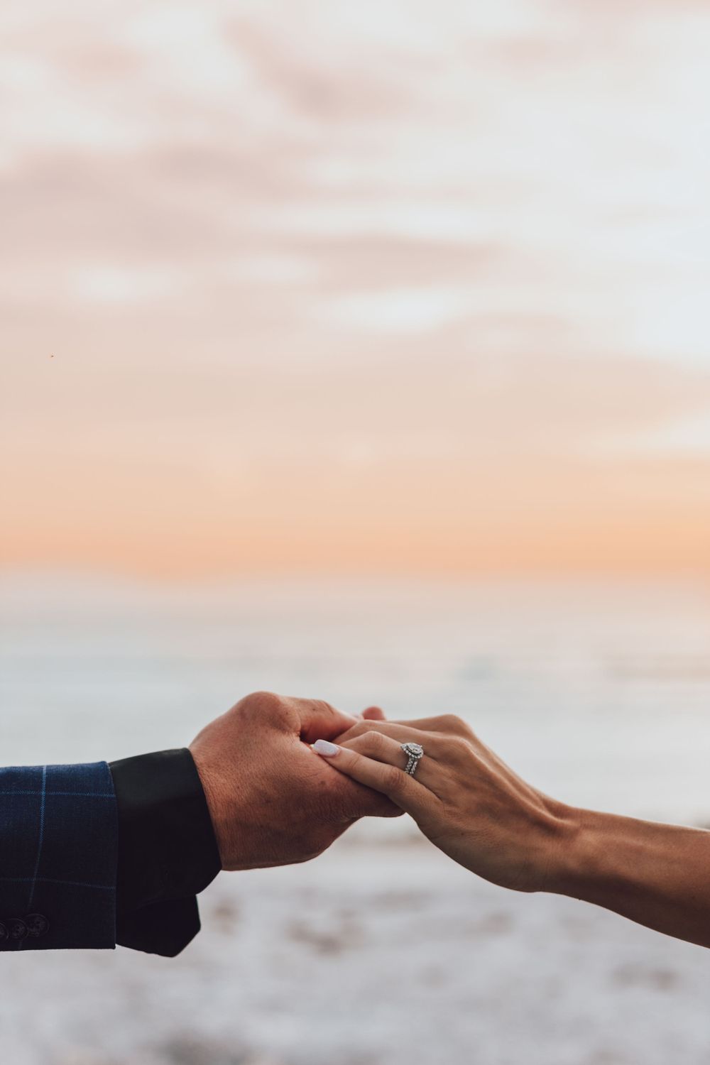 Close up of hands showing wedding ring against sunset sky.