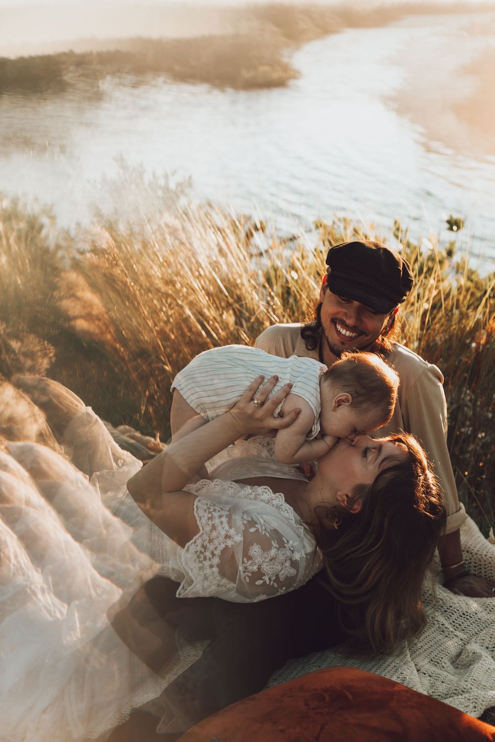 Family sharing tender moment together on blanket by lake during sunset.
