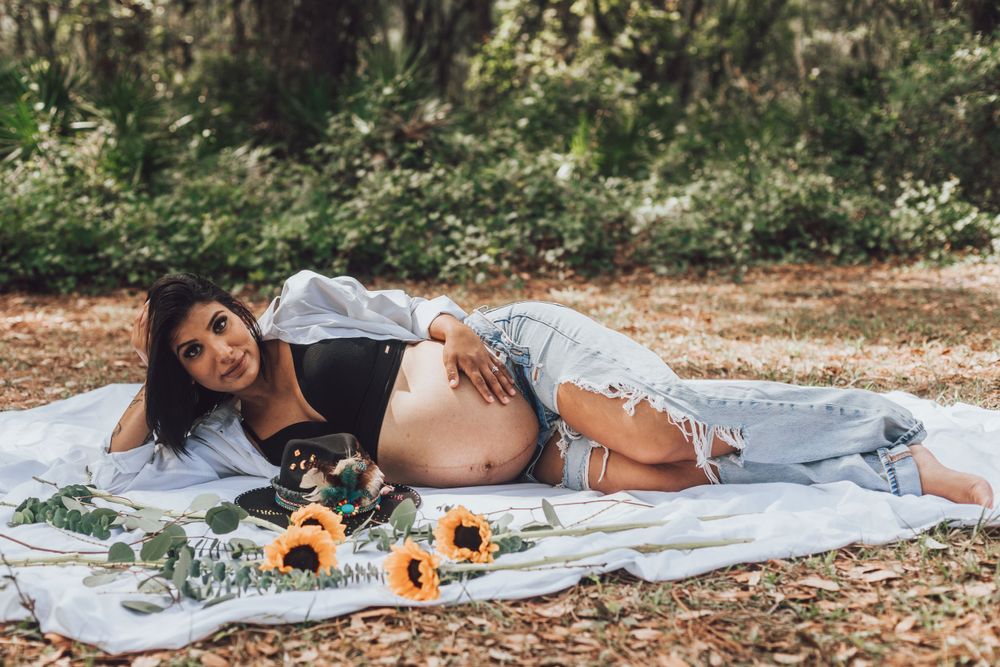 Outdoor maternity photo with sunflowers and eucalyptus on white blanket.