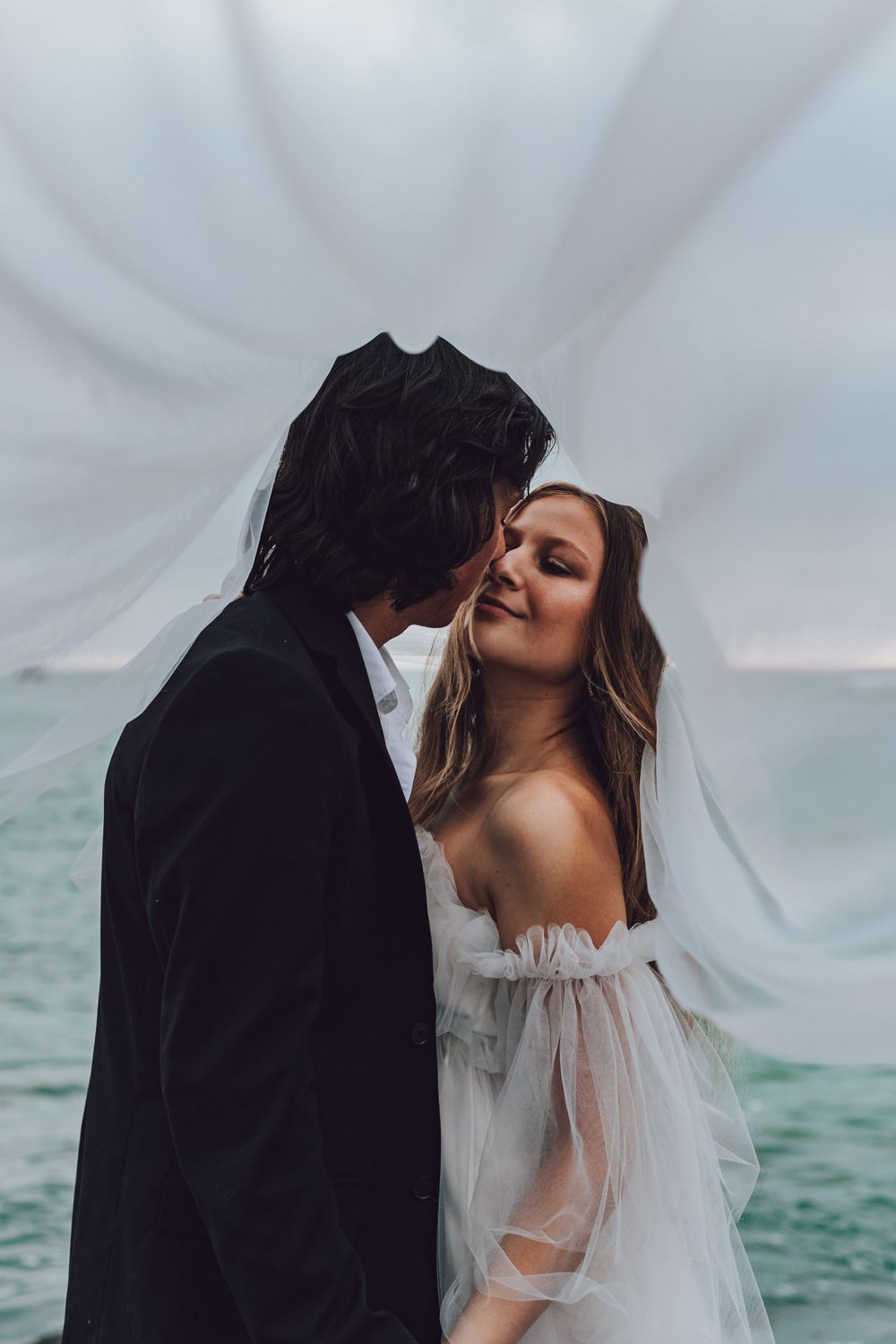 Romantic seaside moment with flowing veil and turquoise ocean waters in the background.
