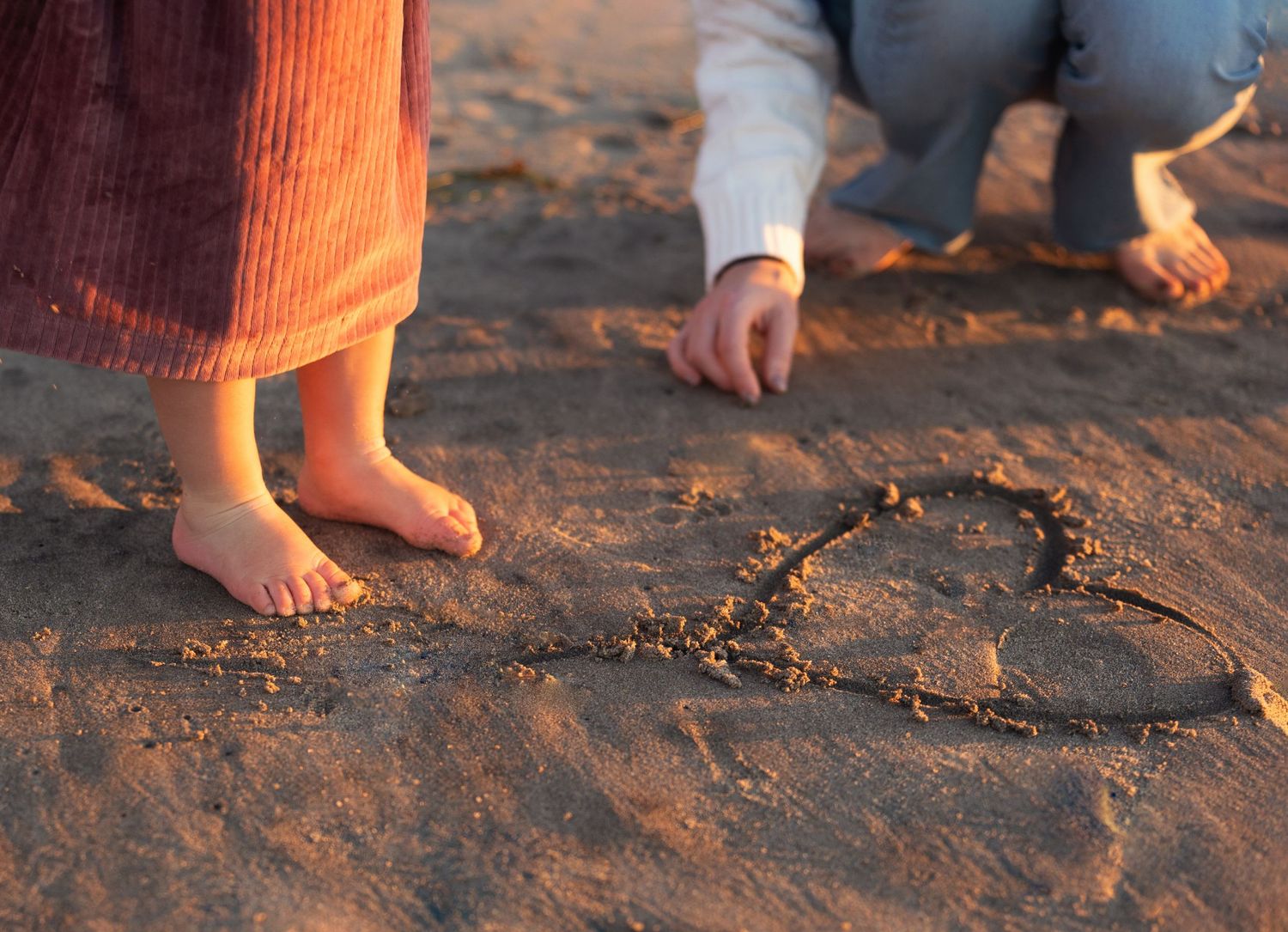 Bare feet near a heart drawn in sand during golden hour.