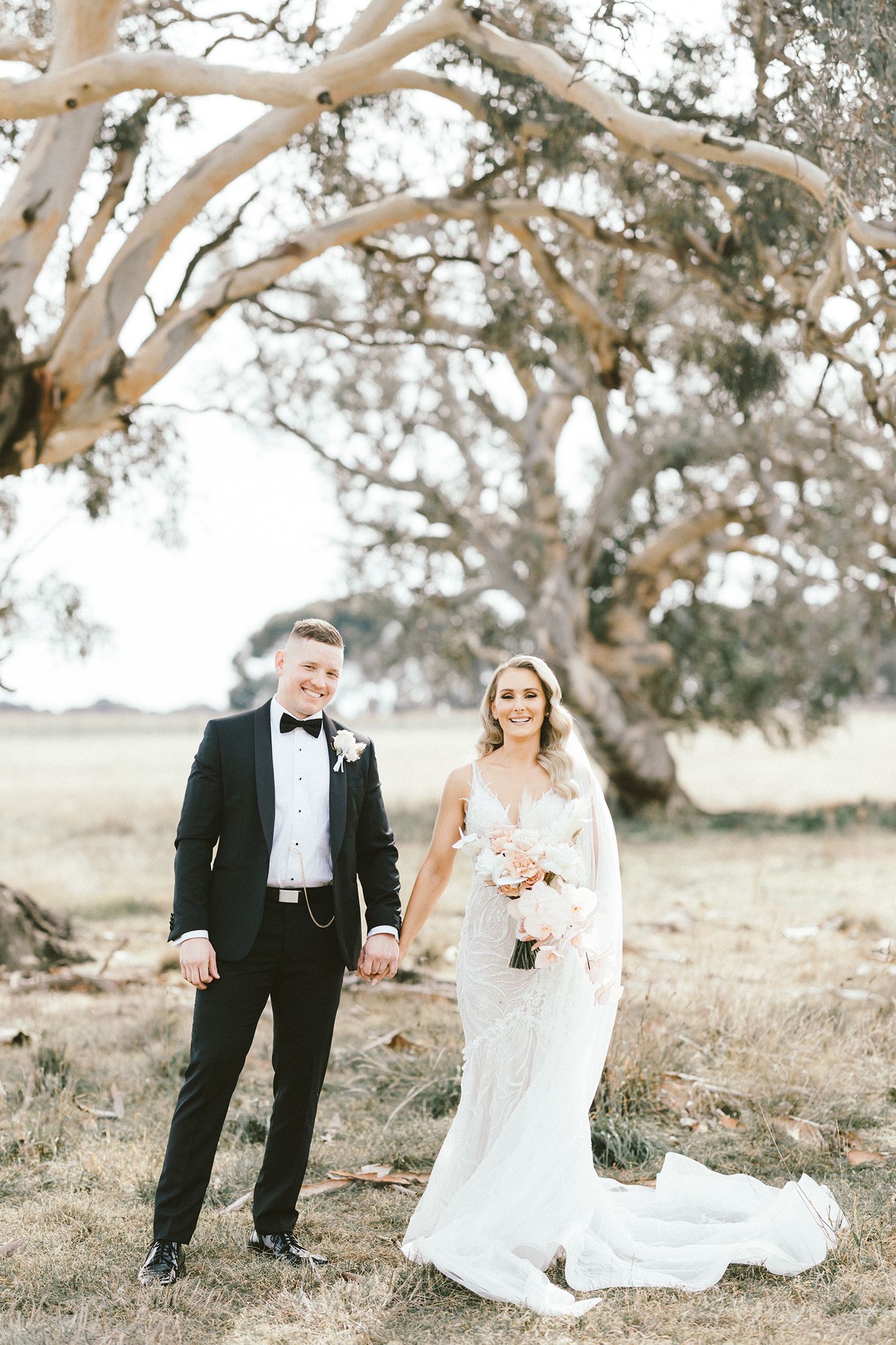 Elegant wedding photography featuring classic formal attire against backdrop of majestic tree.