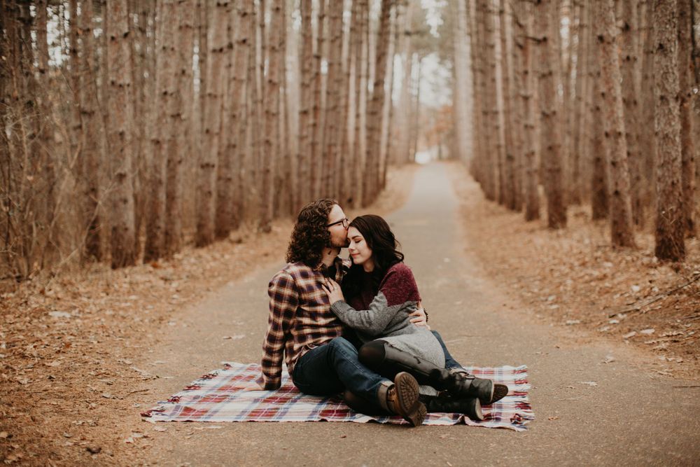 Couple cuddling playfully on plaid blanket along a quiet autumn forest path.