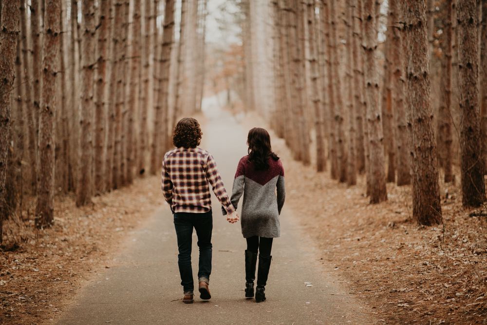 Couple walking hand in hand down a scenic tree-lined path in an autumn forest.