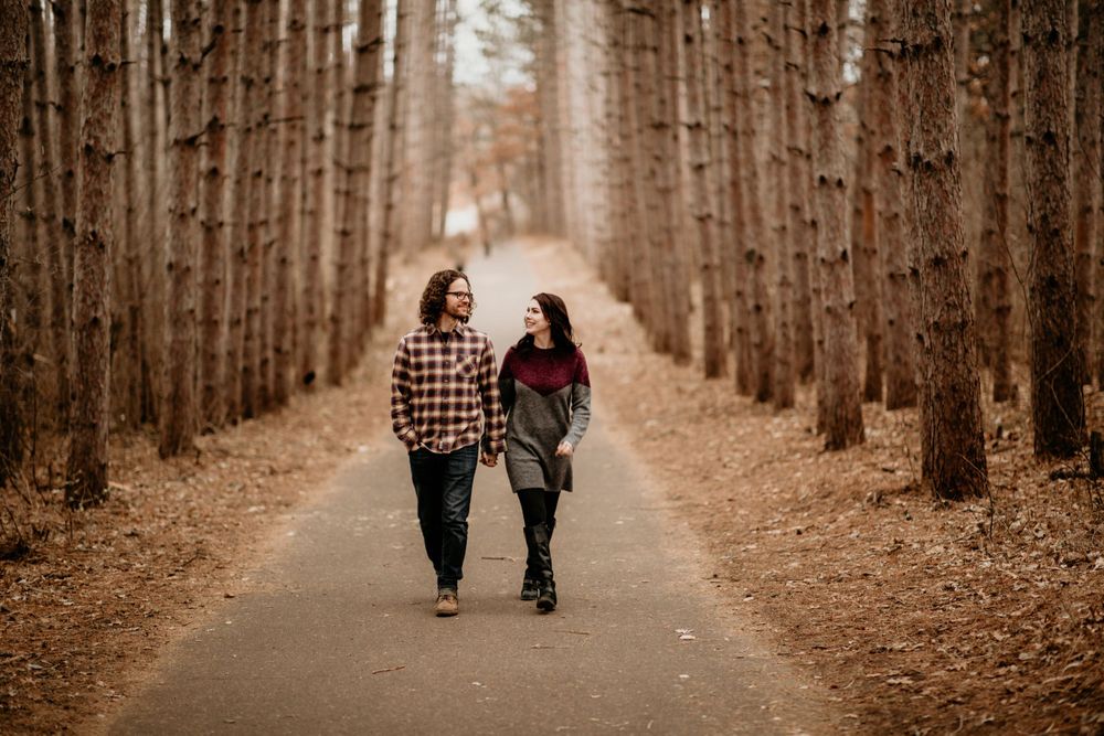Couple strolling hand in hand, smiling at each other on a fall forest path.