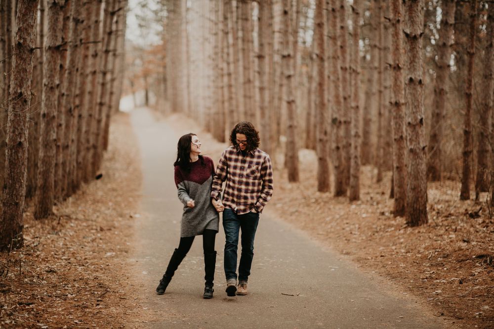 Couple walking hand in hand down a tree-lined path in an autumn forest.