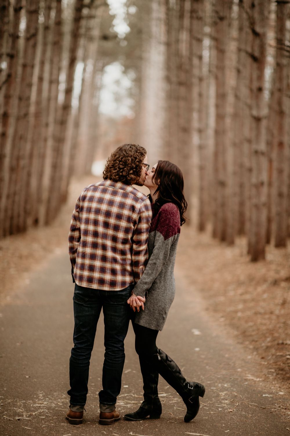 Couple sharing a kiss on a scenic forest path surrounded by tall trees.