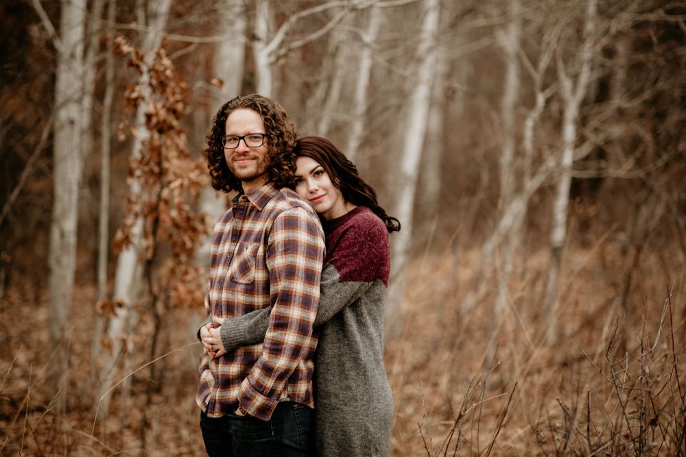 Couple embracing warmly among bare white birch trees in autumn woods.
