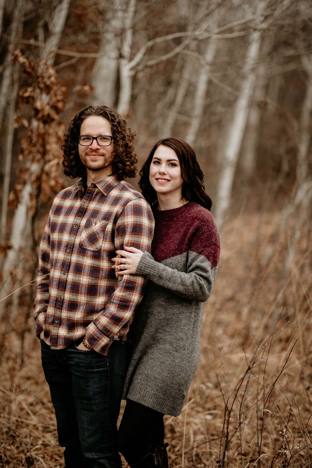 Smiling couple posing together in a woodland setting with bare birch trees.