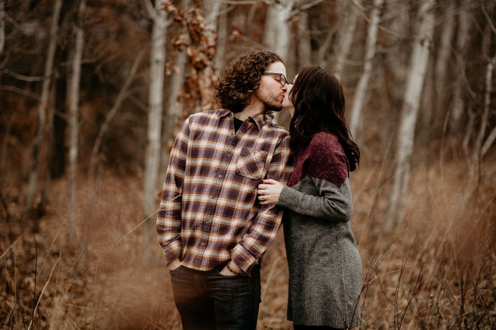 Couple sharing a tender kiss among golden fall foliage in the woods.