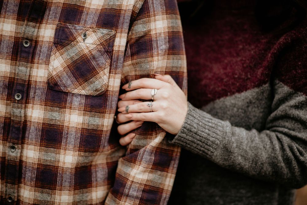 Detail shot of engagement ring as woman holds mans plaid flannel shirt.