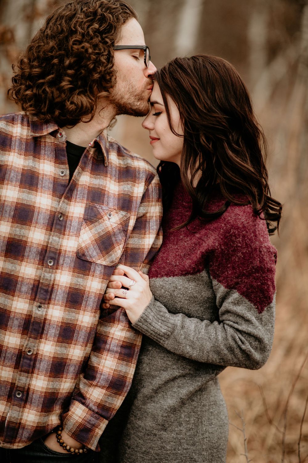 Romantic couple sharing a kiss outdoors in autumn, woman in gray burgundy sweater, man in plaid shirt.