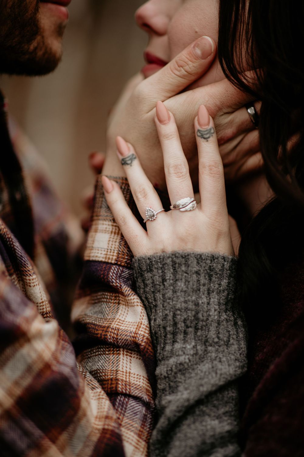 Close-up of woman's hand with tattoos and engagement ring resting on man's plaid shirt collar.