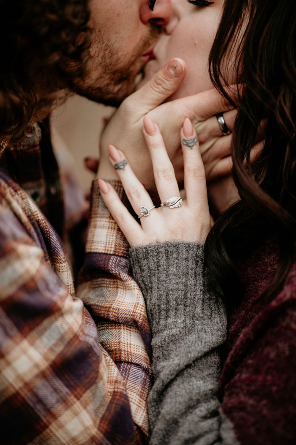 Close-up of couple kissing with woman's tattooed hand displaying engagement and stacked rings.