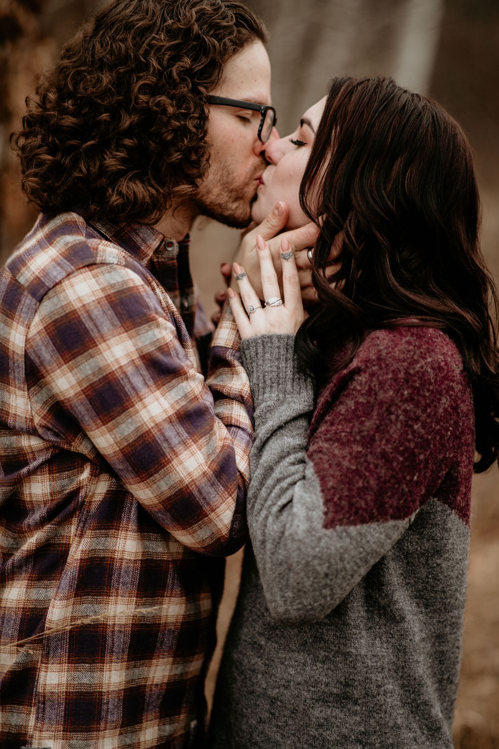 Engaged couple kissing passionately in fall setting, woman showing off diamond engagement ring.