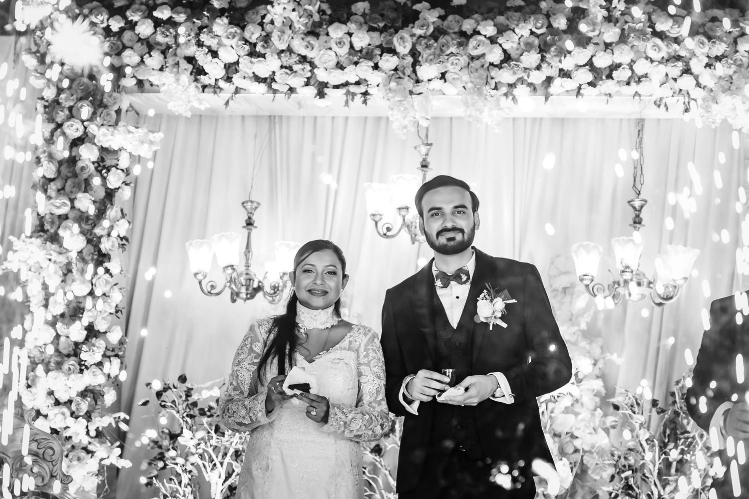 Black and white photo of wedding guests celebrating with confetti in an elegant venue.