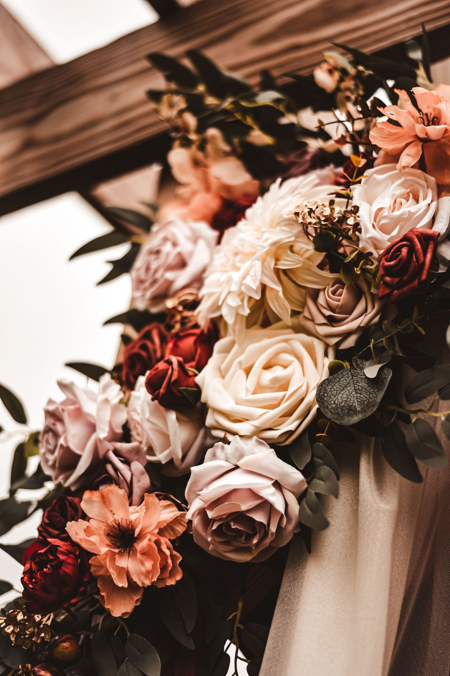 Romantic floral arrangement with pink and cream roses against wooden backdrop.