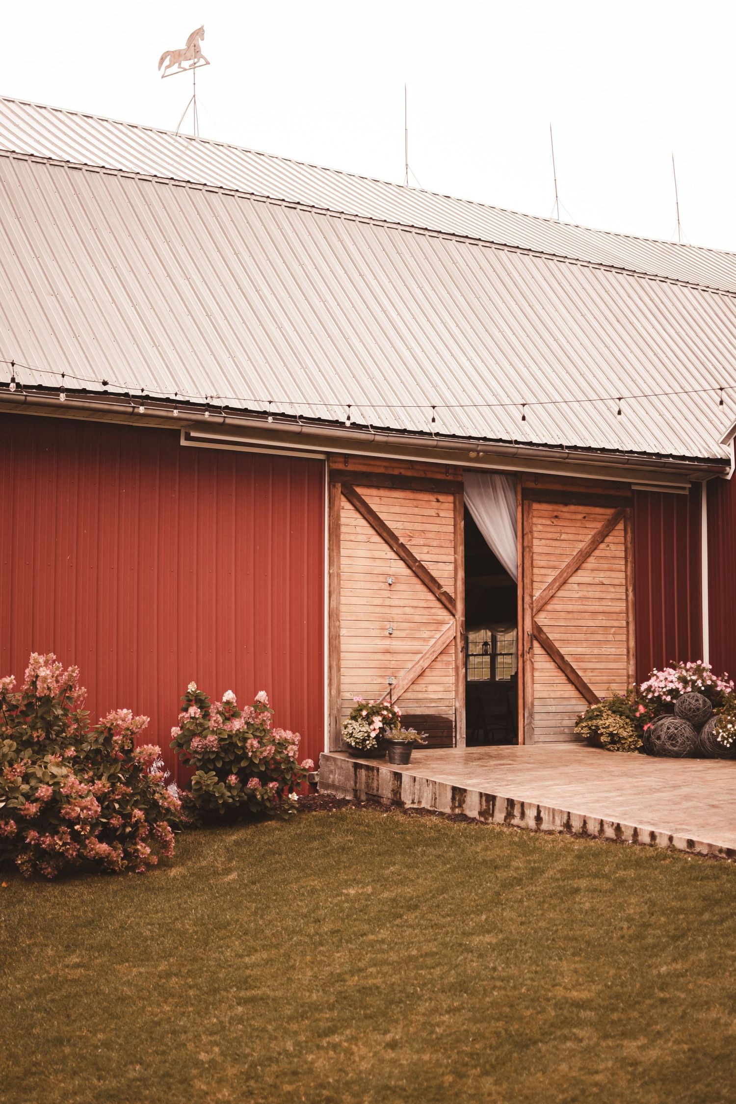 Red barn with wooden sliding doors and pink flowers blooming in front of the entrance.