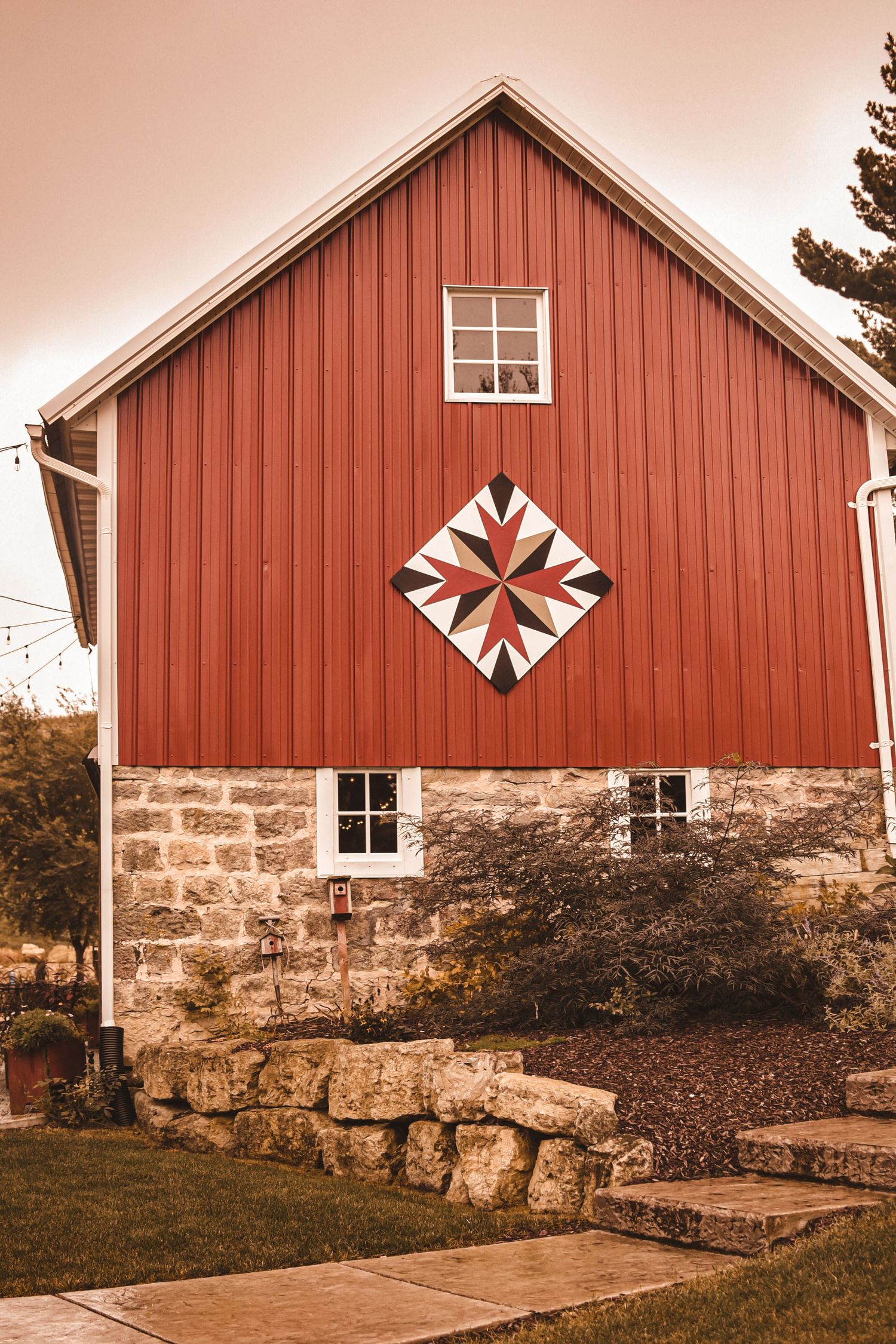 Red barn with stone foundation featuring a decorative quilt pattern on its facade.