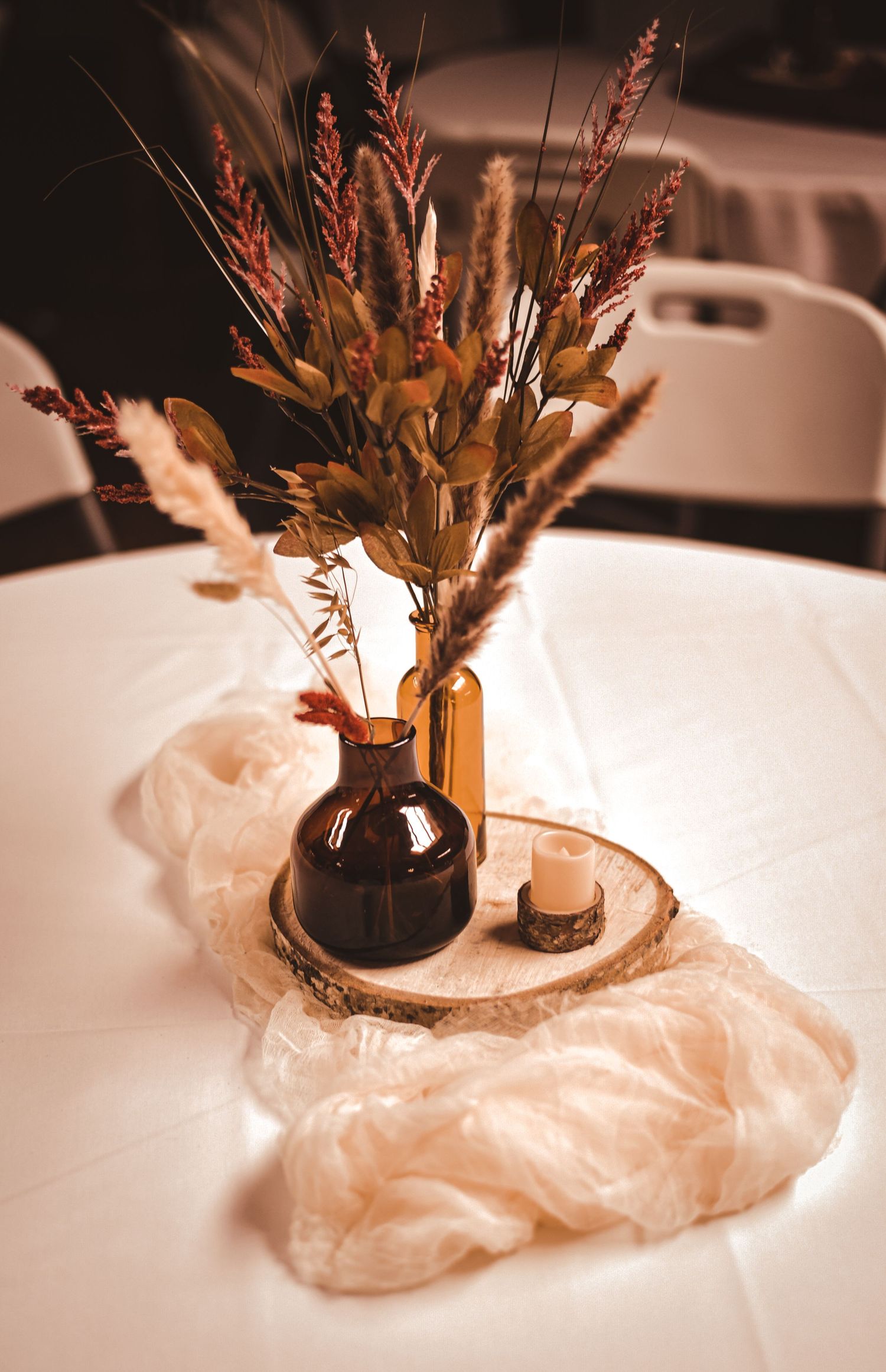 Autumn-colored dried flower arrangement in dark bottle on white tablecloth with tea light.