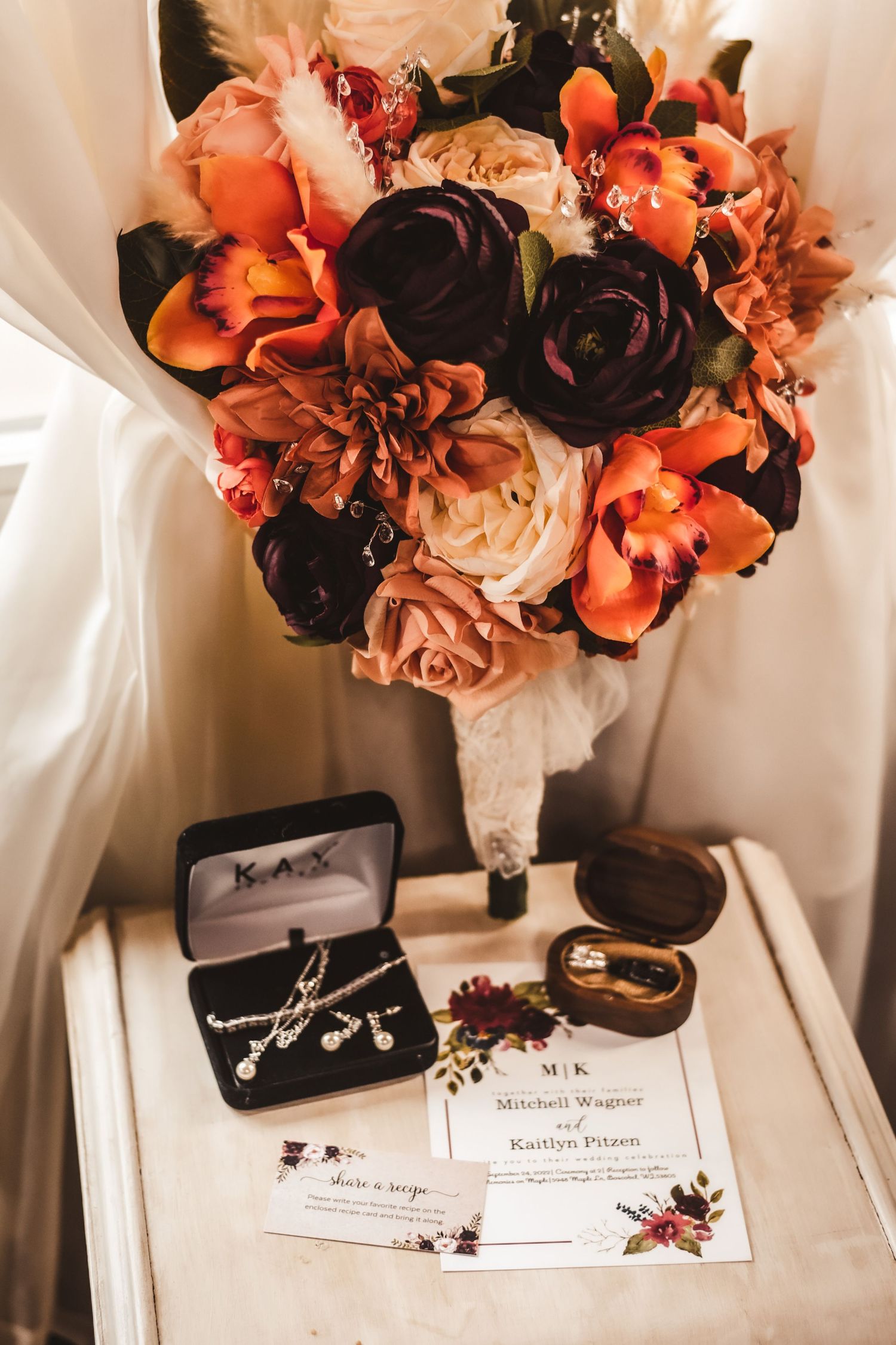 Wedding details featuring orange and burgundy bouquet with jewelry and invitation.