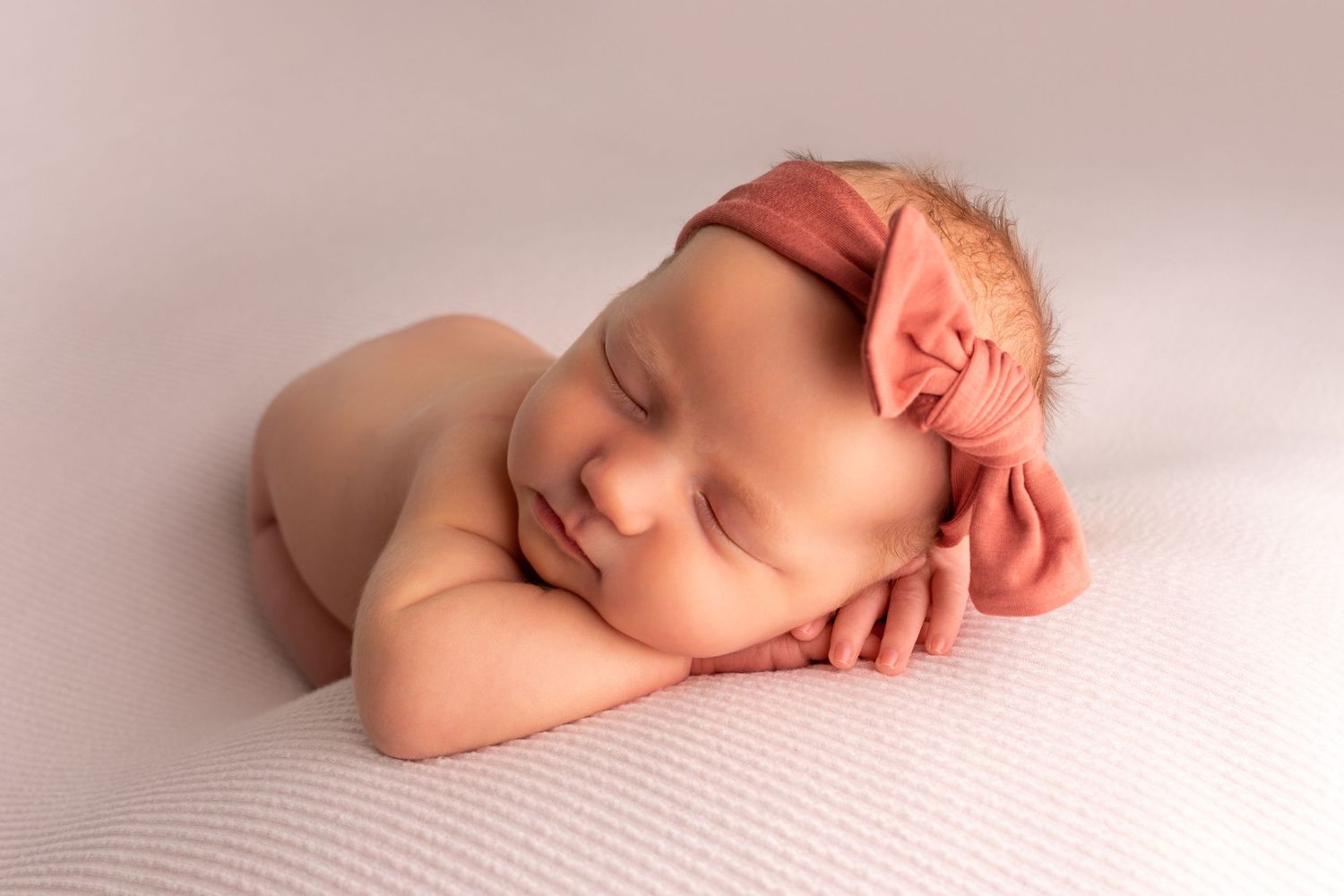Peaceful sleeping newborn wrapped in soft fabric against pink background.